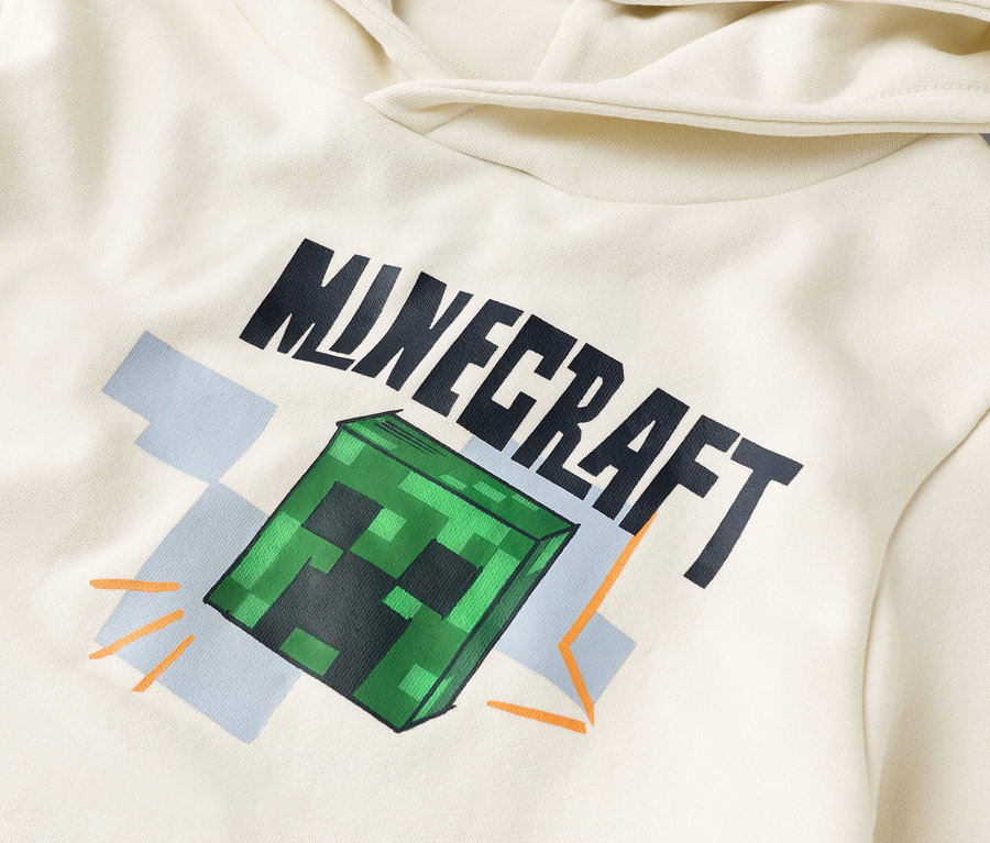 Detailný pohľad na krémovú mikinu s kapucňou s potlačou "Minecraft" a zeleným blokom Creeper.