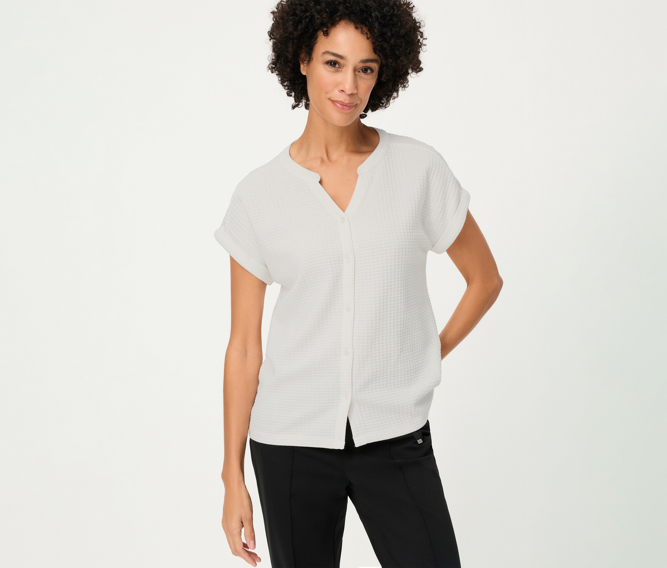 Žena s kučeravými vlasmi má na sebe štruktúrovanú košeľu Olsen s gombíkmi v bielej farbe a čierne nohavice.