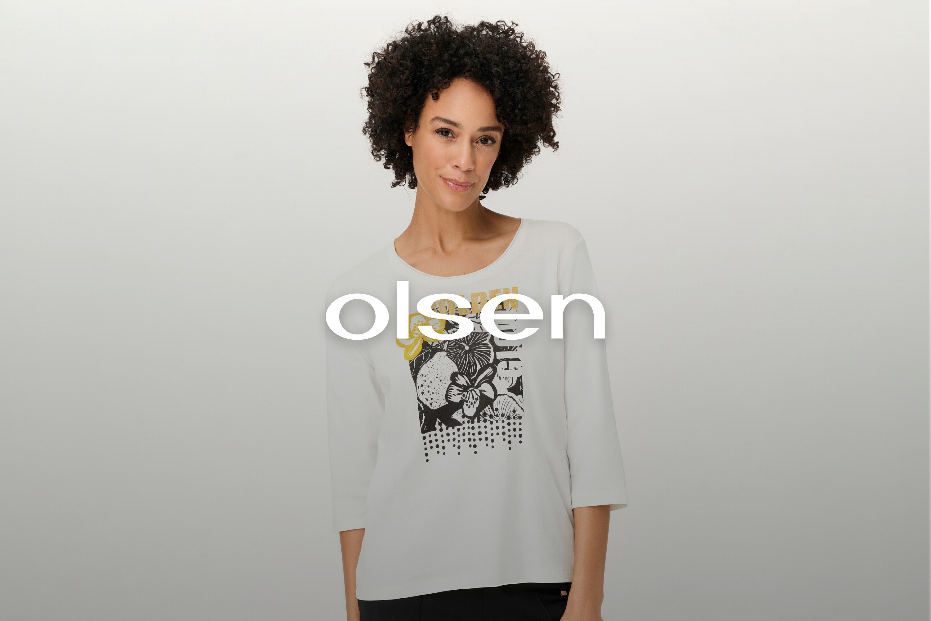 Žena s kučeravými vlasmi má na sebe biele tričko s dlhým rukávom a kvetinovým vzorom.