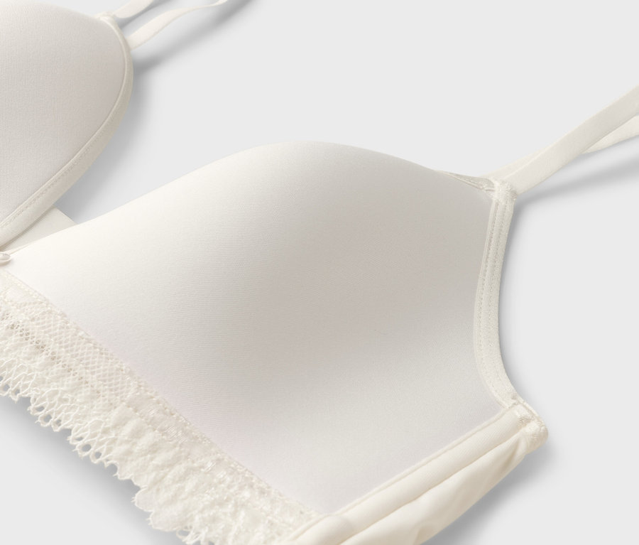 Detailný záber bielej podprsenky s čipkou a tenkými ramienkami.
