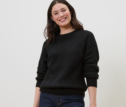 Usmievavá sa žena má na sebe čierny pletený pulóver.