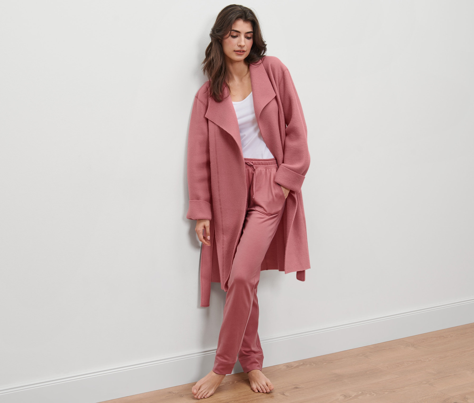Žena opretá o stenu má na sebe jemný flísový kabát a nohavice.