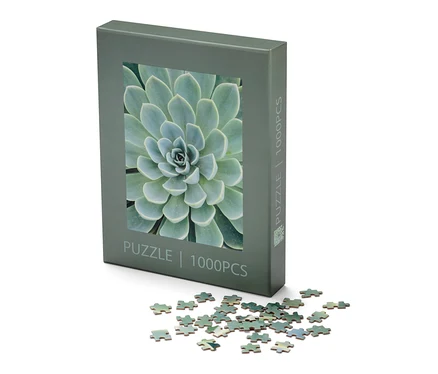 Balenie puzzle »Sukkulente« a niekoľko dielikov puzzle leží na bielom pozadí.