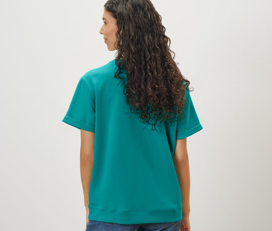 Žena s dlhými vlnitými vlasmi má na sebe akvamarínové tričko zo zmesi modalu a džínsy.