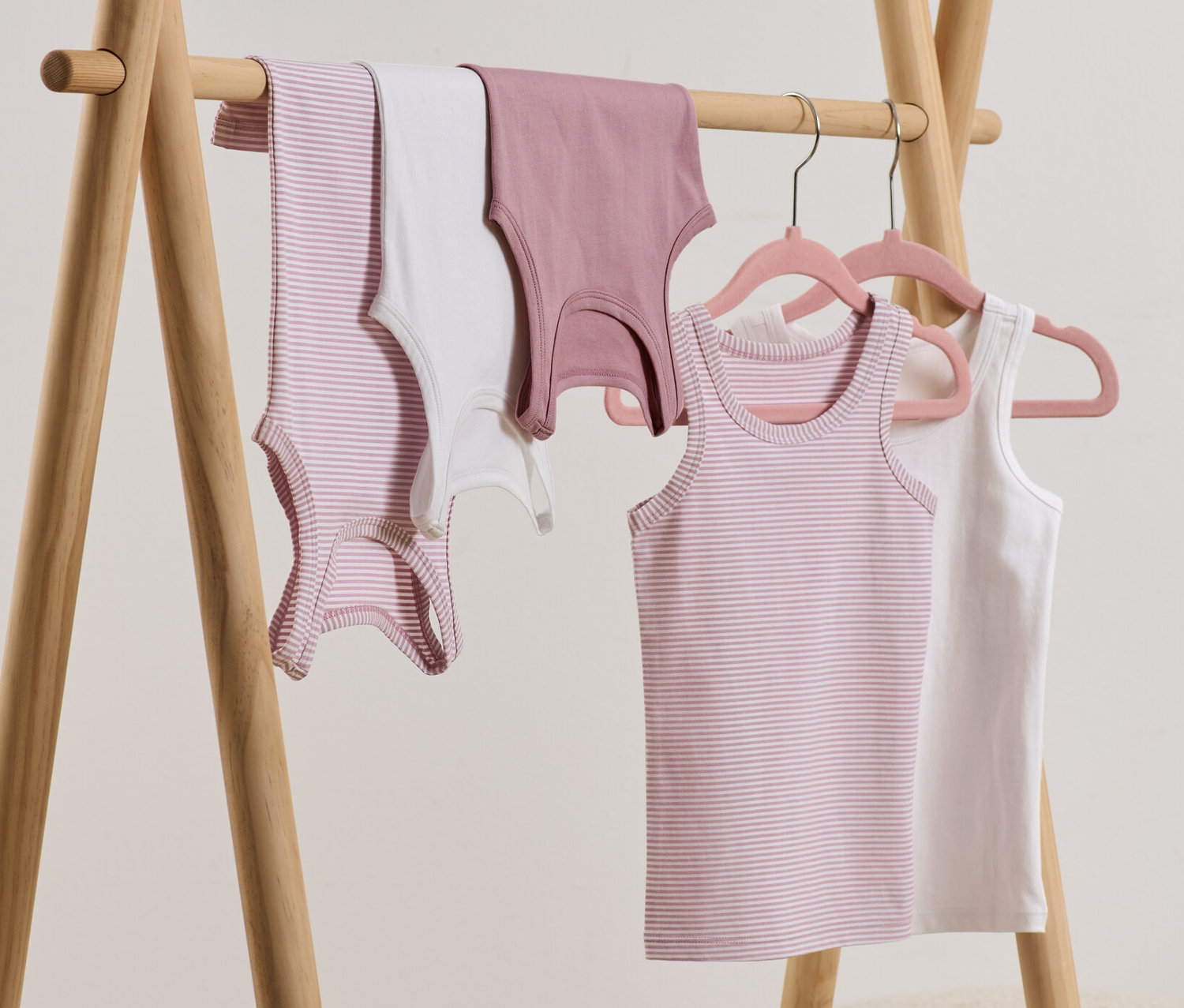 Na drevenom vešiaku visia dievčenské tielka, 5 ks, niektoré sú na vešiakoch.