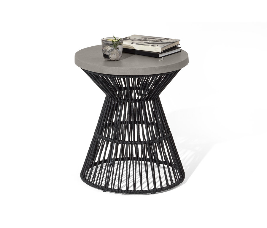 Na odkladacom stolíku s polycementovou stolovou doskou a textilným výpletom leží pohár s nápojom a dve knihy.