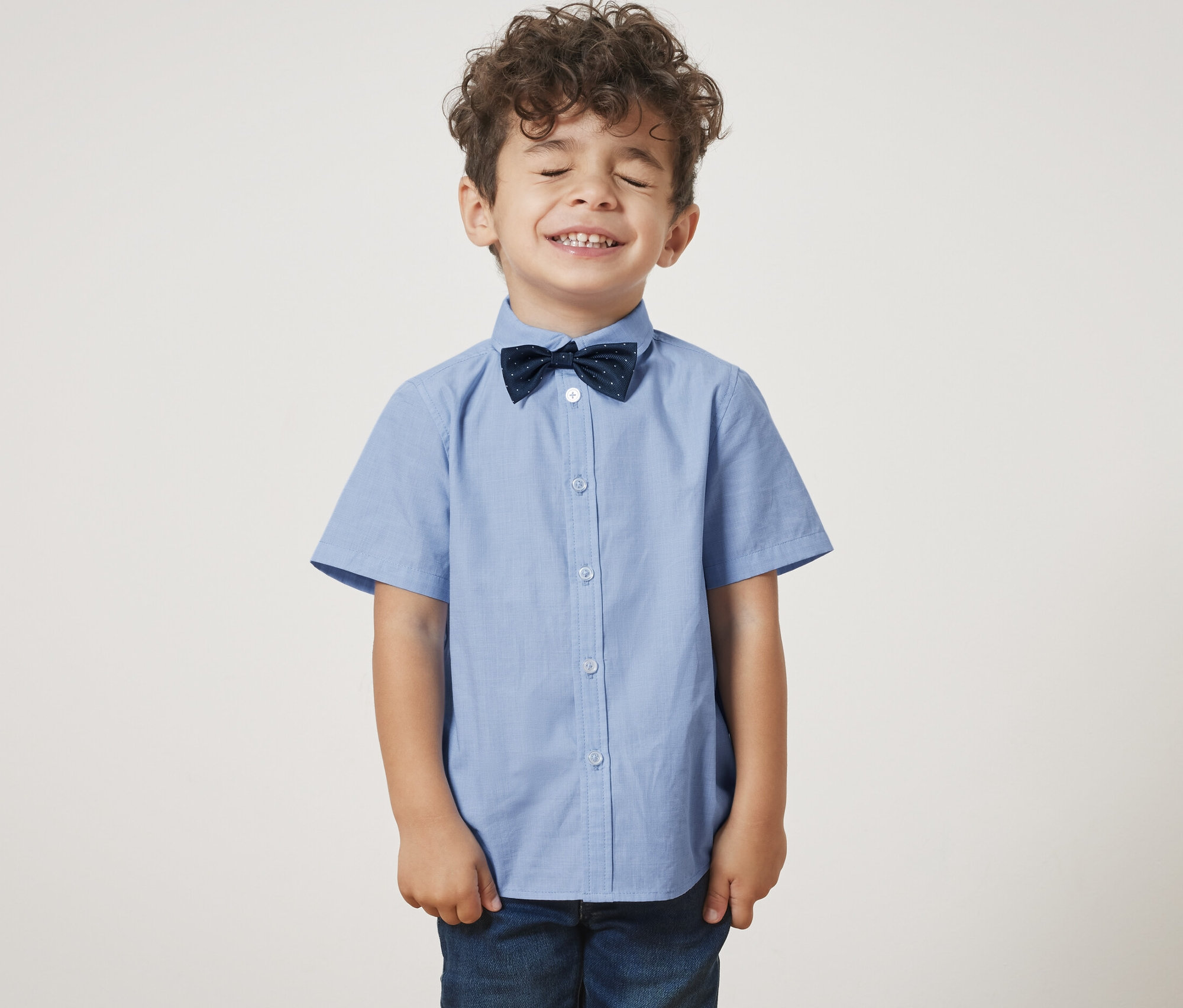 Chlapec so zatvorenými očami má na sebe detskú košeľu s motýlikom.