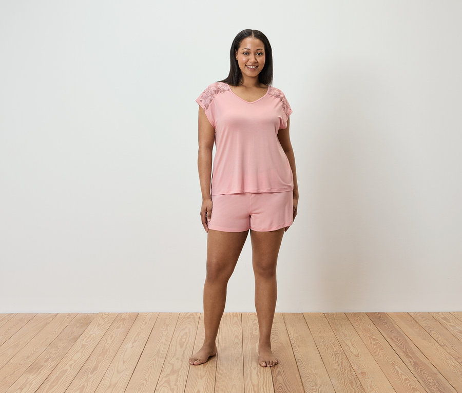 Žena stojí a má na sebe ružové pyžamo s čipkou na ramenách.