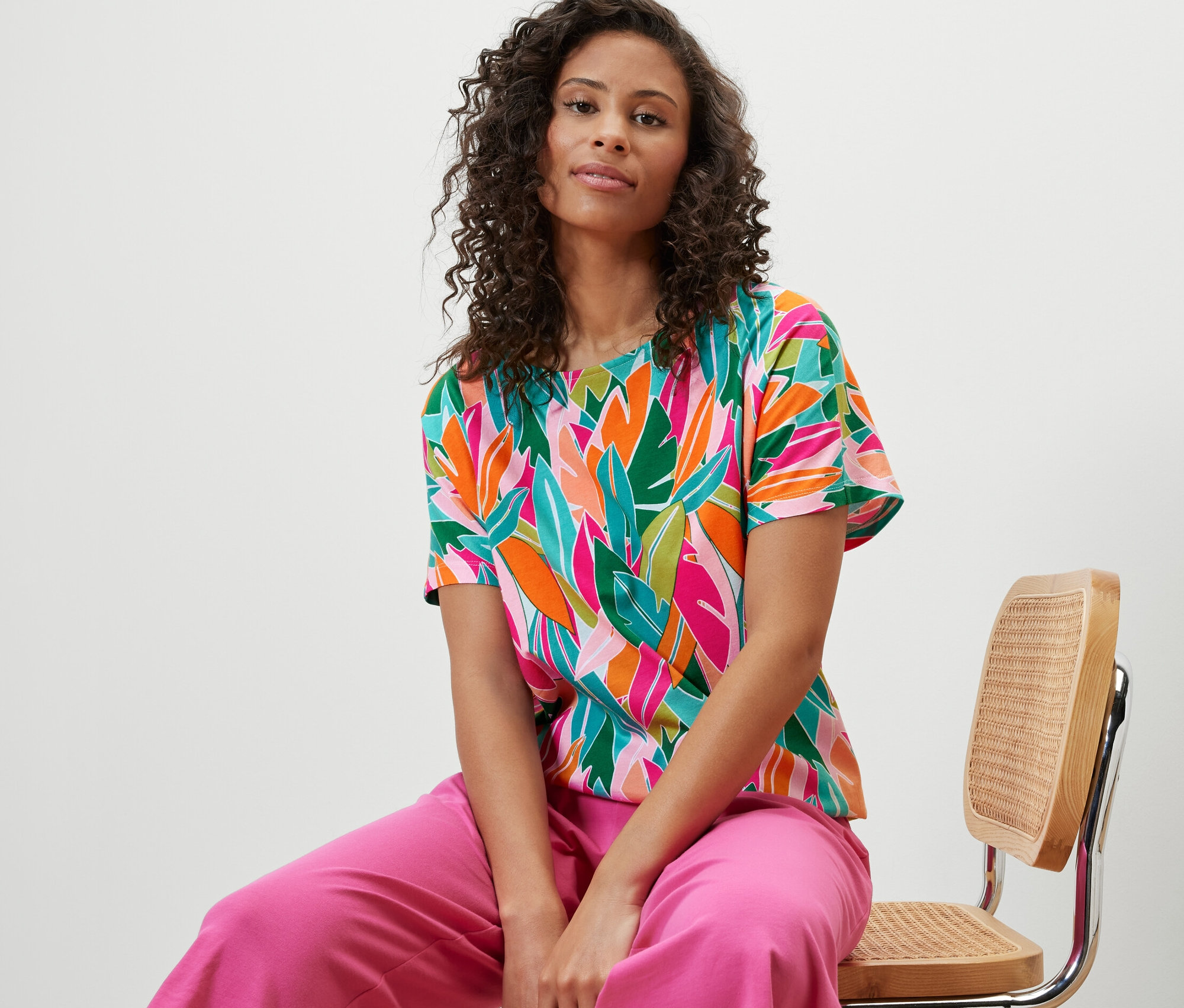 Žena sedí na stoličke a má na sebe spadnuté blúzkové tričko s celoplošnou potlačou.