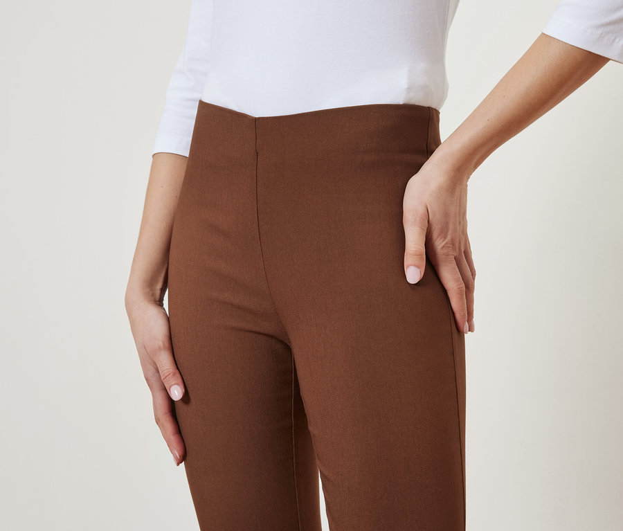 Žena pózuje v hnedých nohaviciach a bielom tope.