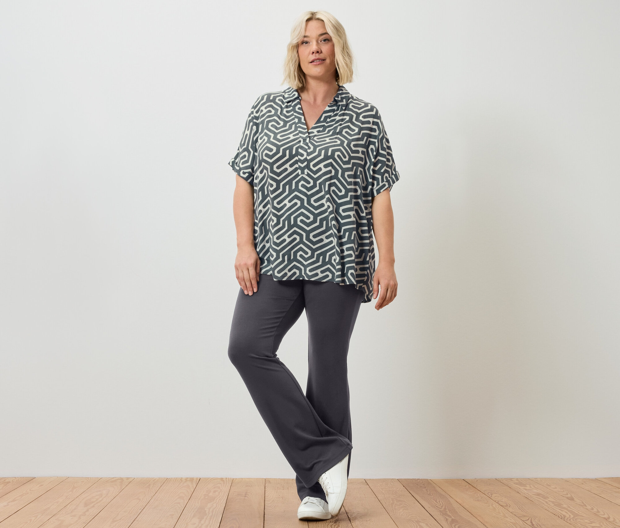 Žena pózuje v rozšírených legínach a blúzke s potlačou.