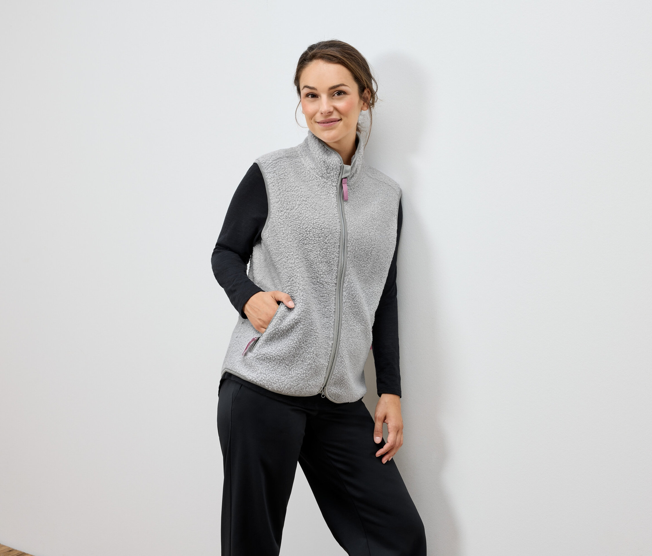 Žena má na sebe sivú flísovú vestu a čierne nohavice.