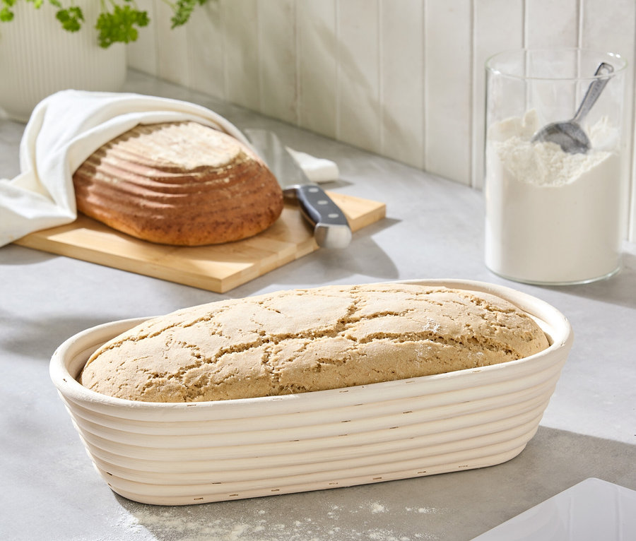 Chlieb v ošatke na linke vedľa múky a chleba na doske na krájanie.