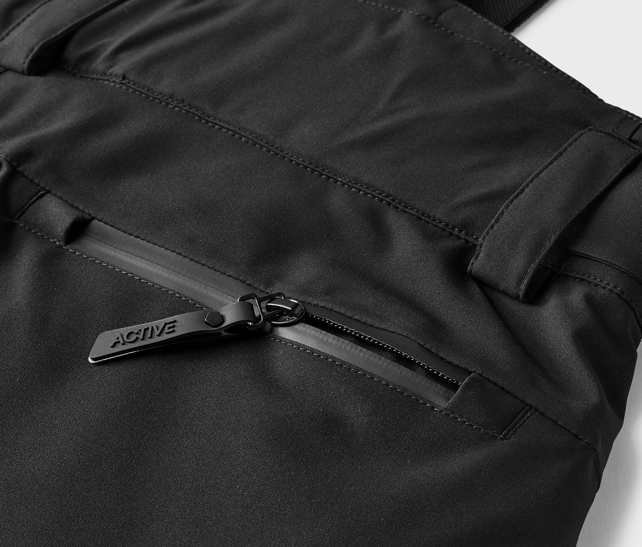 Detail čiernych nohavíc s vreckom na zips s jazdcom s nápisom ACTIVE.