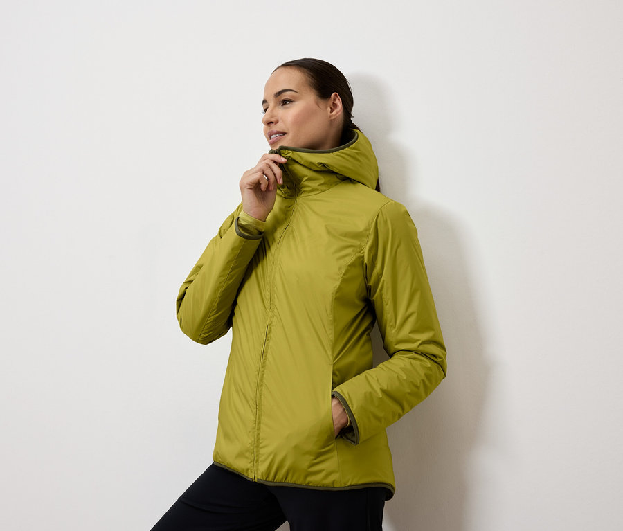 Žena si zapína žltozelenú bundu s kapucňou.