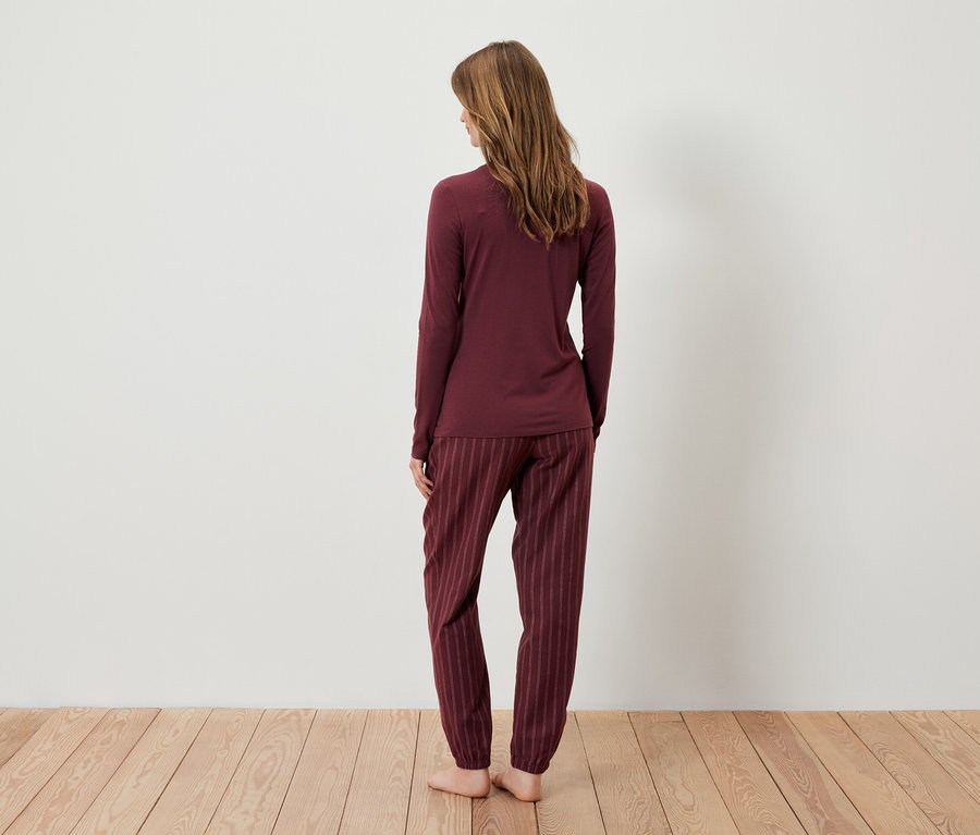 Žena stojí chrbtom k fotoaparátu a má na sebe bordové pyžamo.