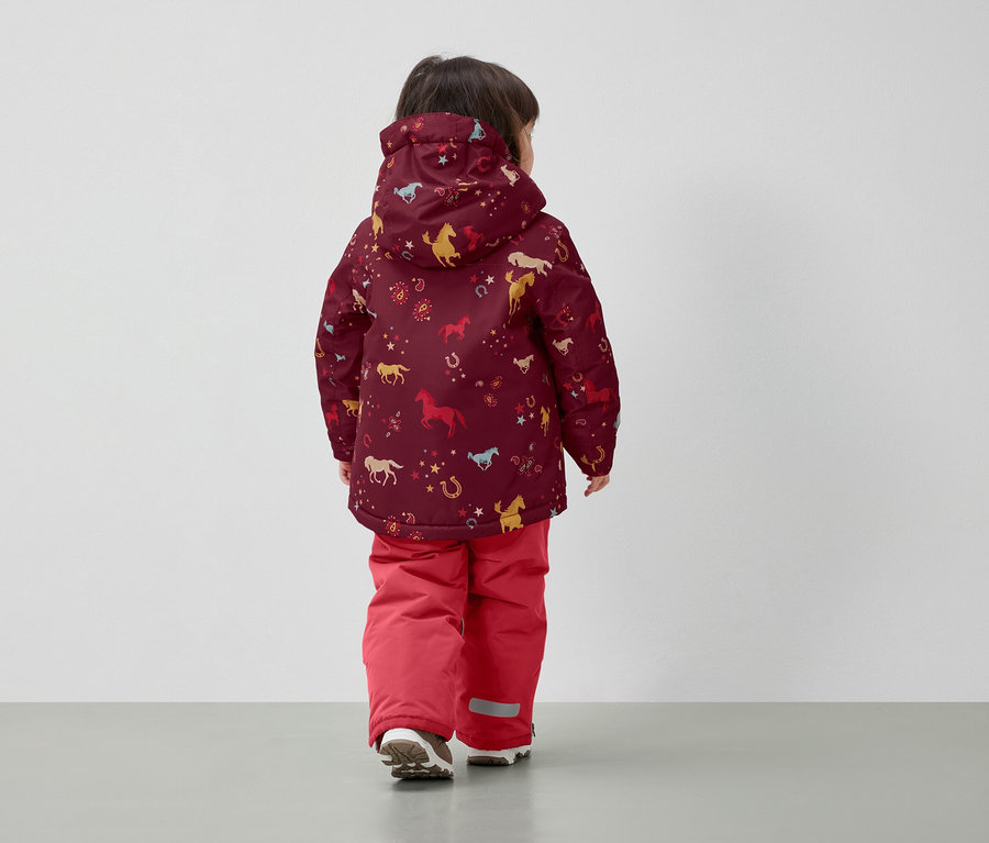 Chlapec v zimnej bunde s potlačou koní a červených nohaviciach, chrbtom k fotoaparátu.