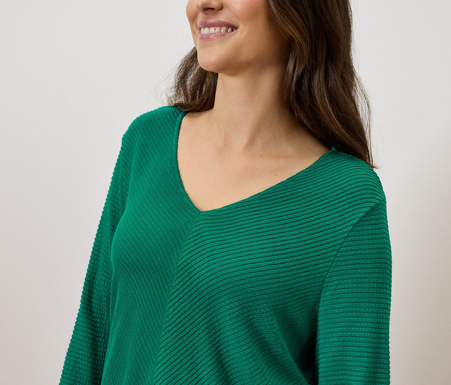 Usmievavá sa žena s hnedými vlasmi v zelenom svetri s výstrihom do V.