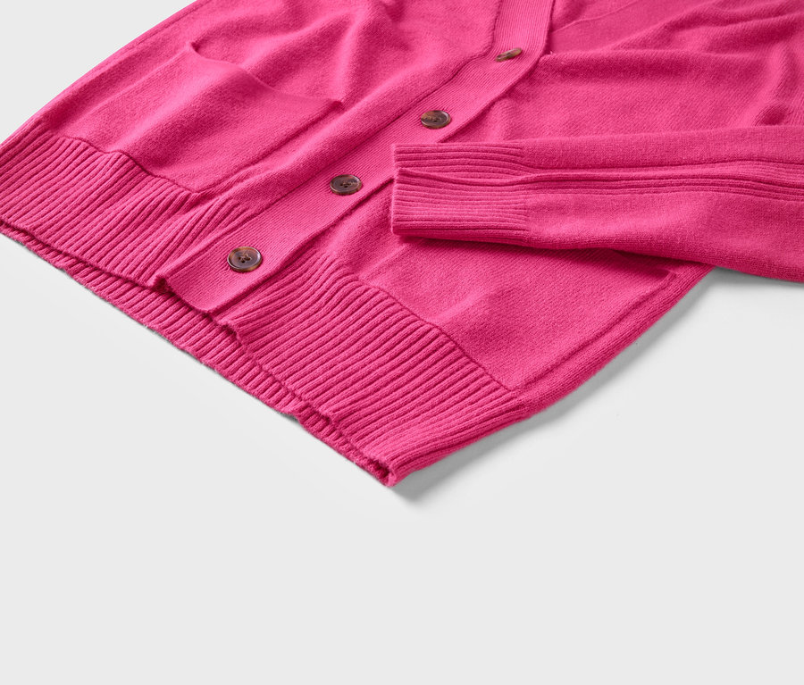 Detail ružového svetra s gombíkmi a vreckom.