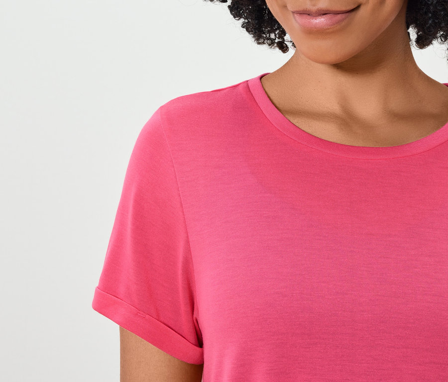Horná časť tela ženy s tmavými vlasmi v ružovom tričku s krátkym rukávom.
