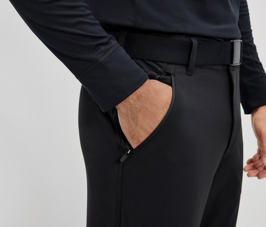 Muž má ruku vo vrecku čiernych nohavíc s opaskom.