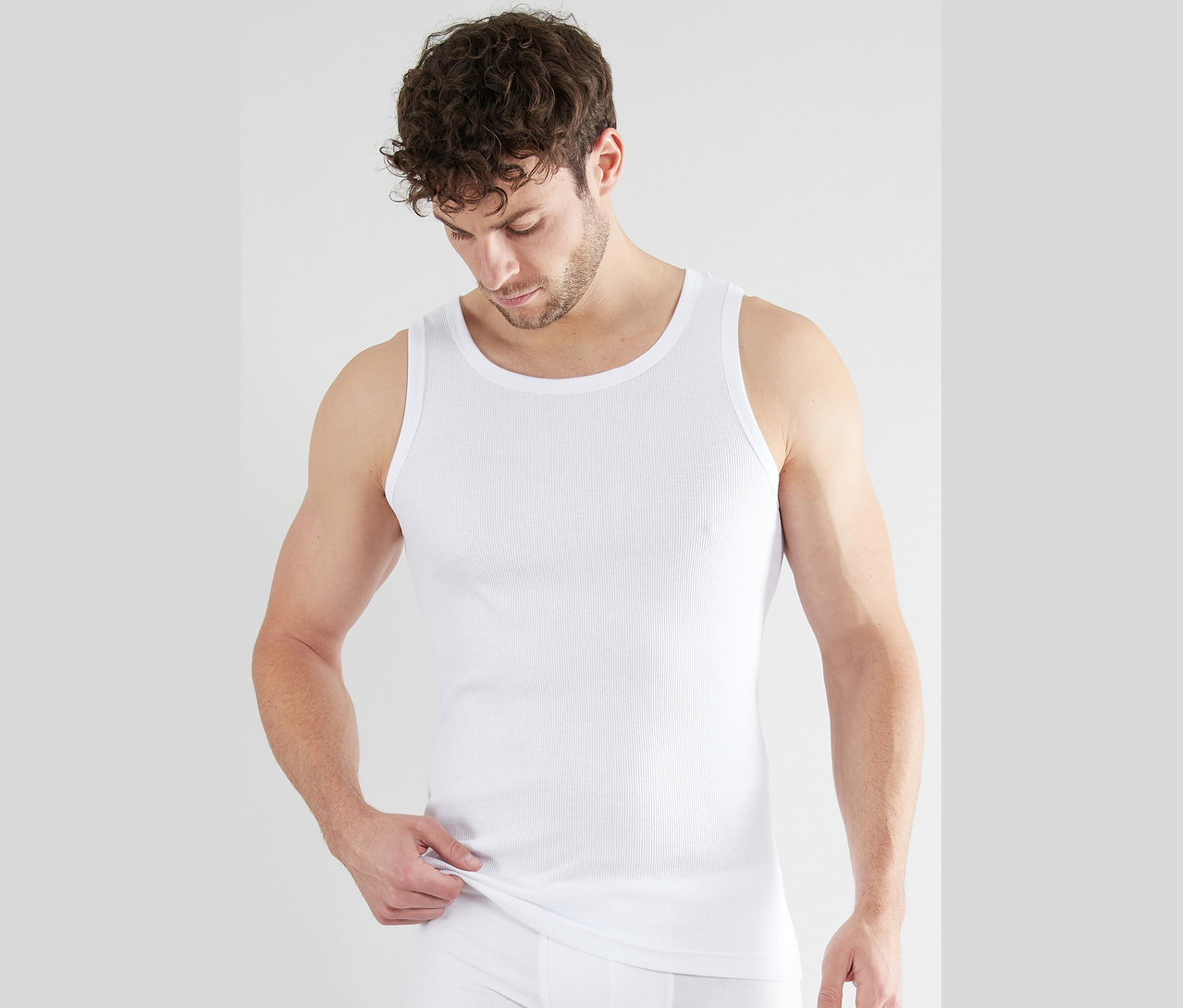 Muž má na sebe biele rebrované tielko a slipy.