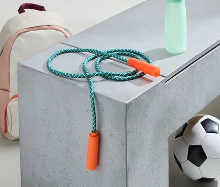 Ružovo-biely batoh, švihadlo, fľaša na vodu a futbalová lopta ležia na sivej lavičke.