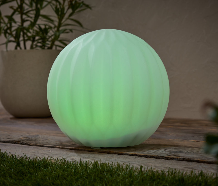Zelená guľovitá lampa stojí na drevenom povrchu vedľa črepníkovej rastliny.