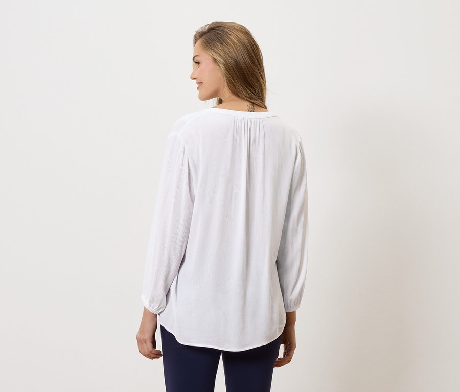 Žena zozadu, má na sebe dlhú, bielu blúzku a modré nohavice.