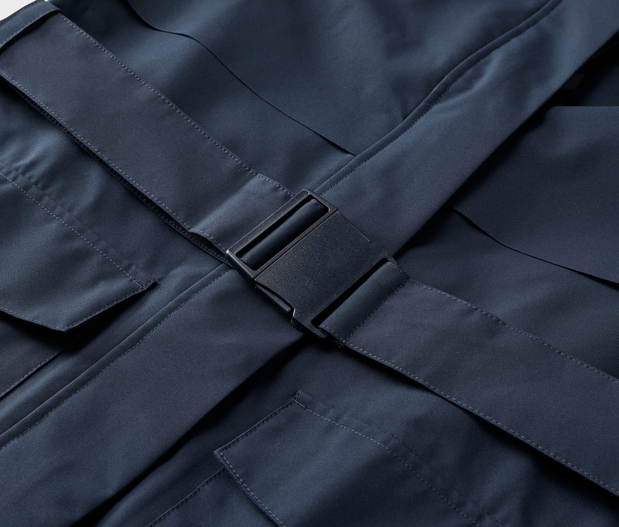 Detailný záber na tmavomodrú bundu s vreckami a čiernym zapínaním na pracku.