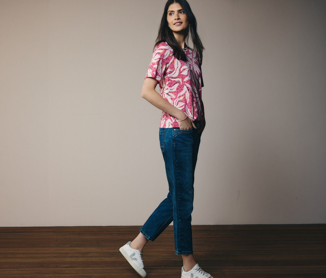 Žena kráča v ružovom tričku s krátkym rukávom CECIL a džínsoch. Ruky má vo vreckách.