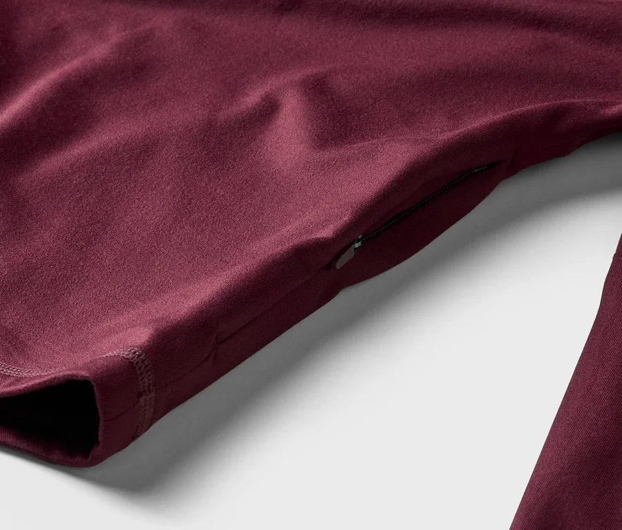 Detail bordového trička s dlhým rukávom a vreckom na zips na rukáve, ležiaceho na bielom pozadí.