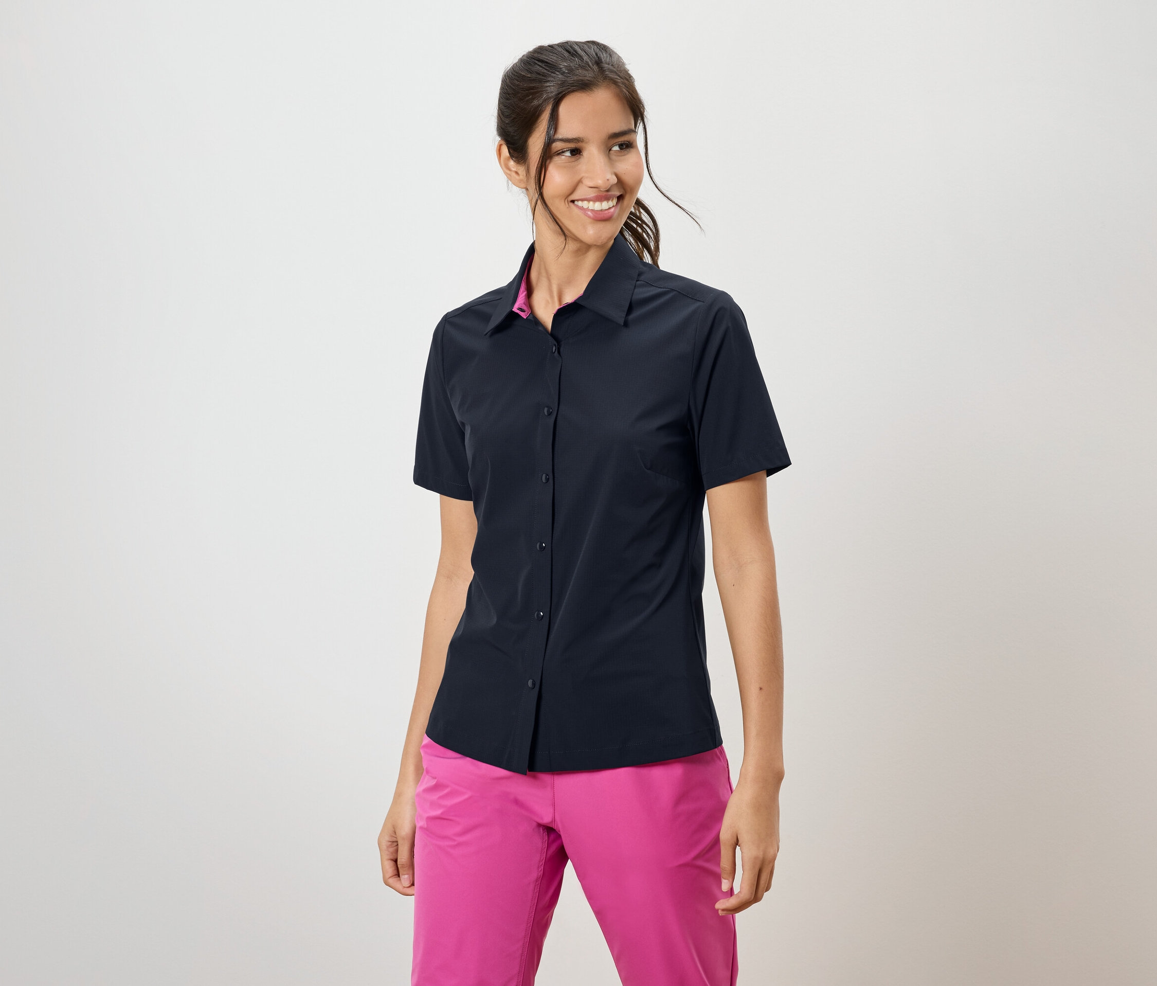 Žena má na sebe tmavomodrú košeľu s krátkym rukávom a ružové nohavice.