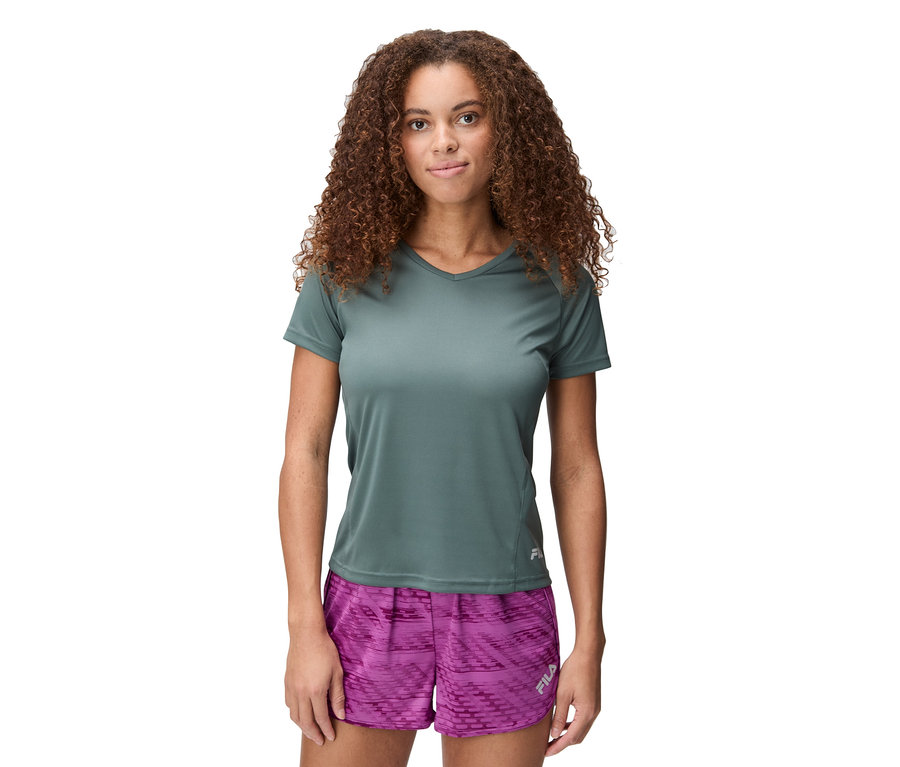 Žena s kučeravými vlasmi má na sebe sivé tričko a ružové šortky.