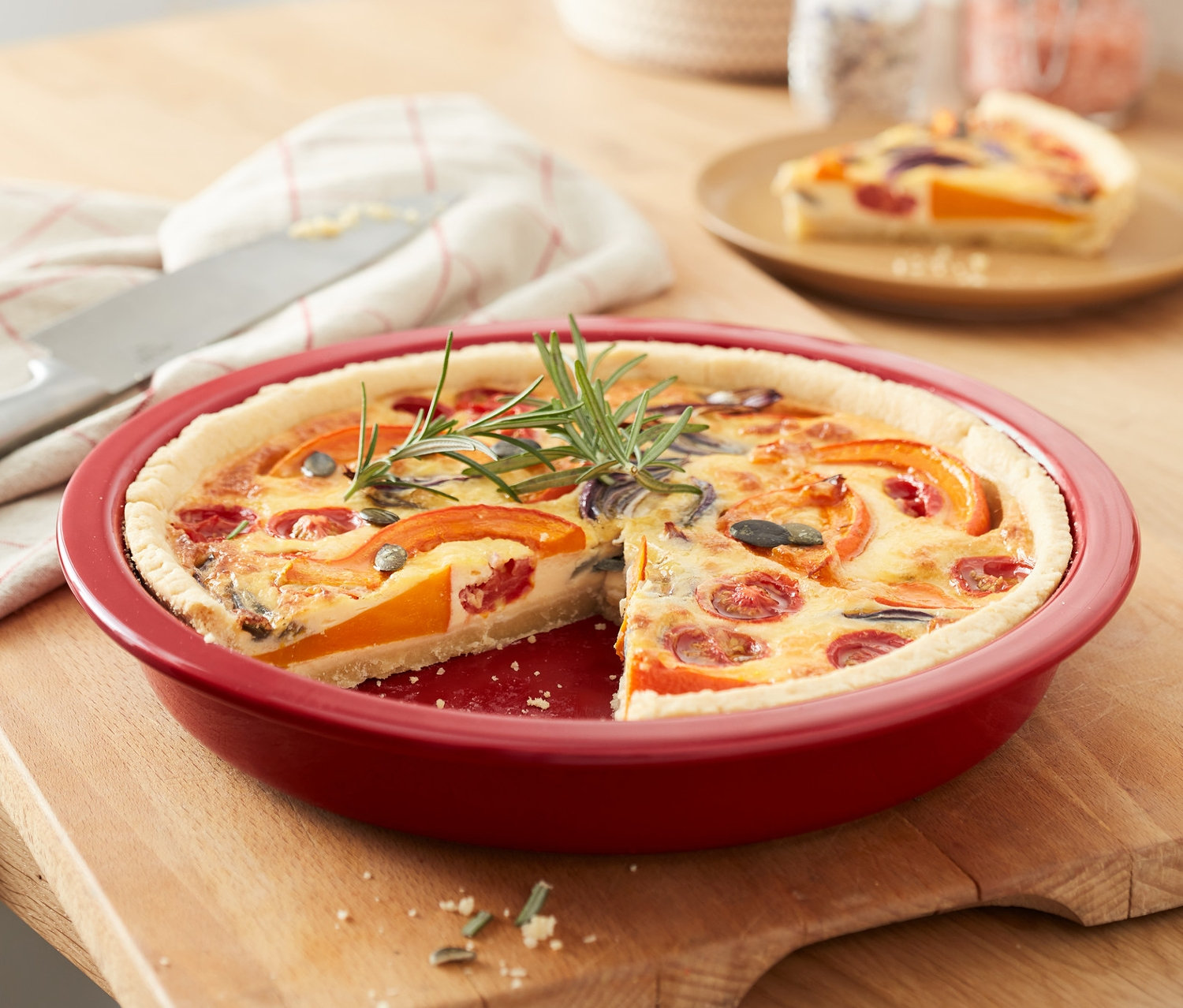 Červená forma na tarte s kúskom tarte na drevenom stole.