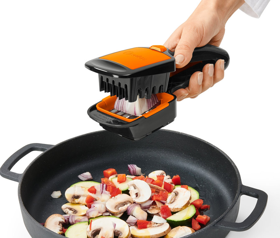 Ruka používa krájač Nicer Dicer Quick XXL na krájanie cibule nad panvicou so zeleninou.