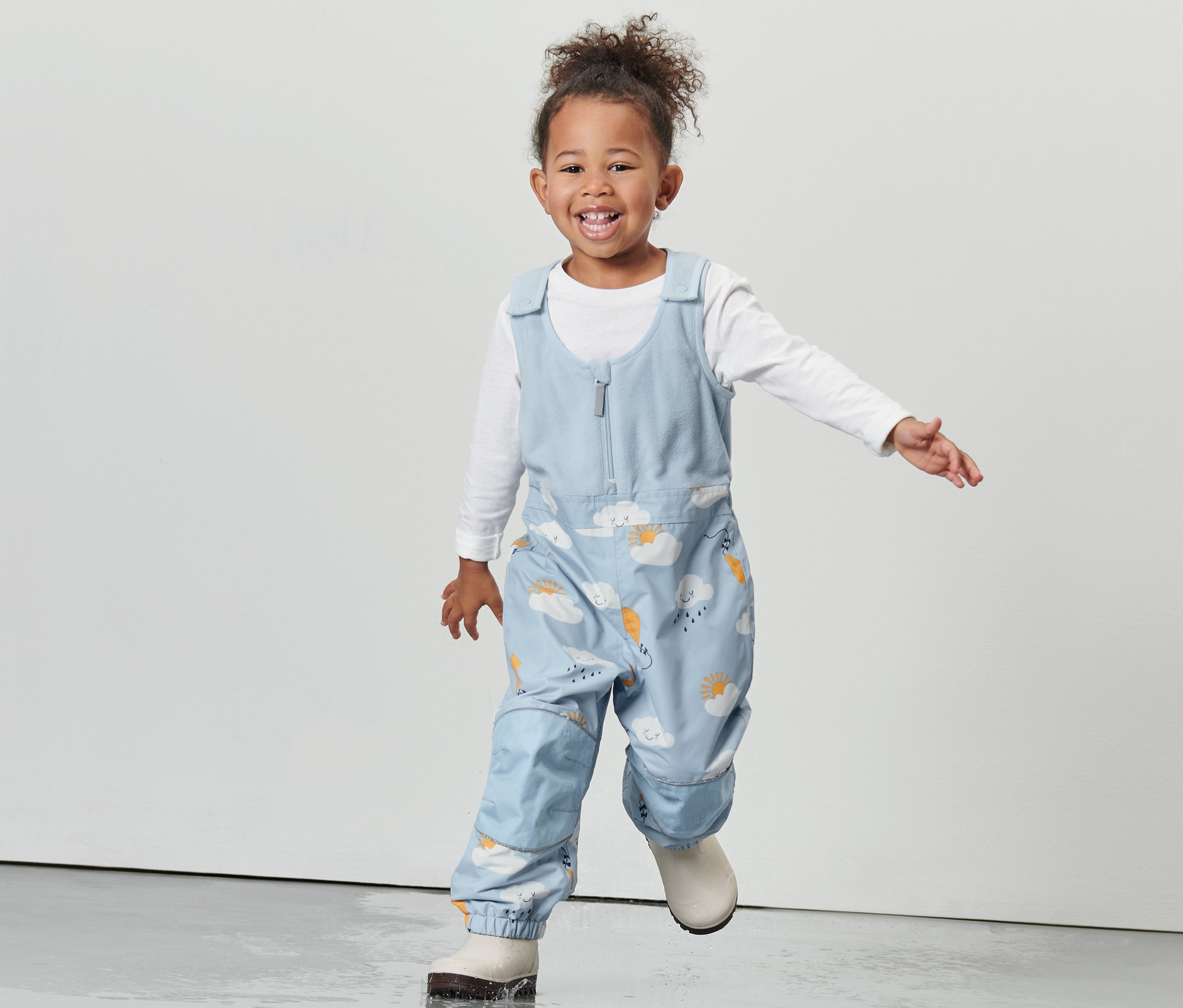 Usmievajúce sa dievčatko v detských termonohaviciach do dažďa s potlačou mrakov.