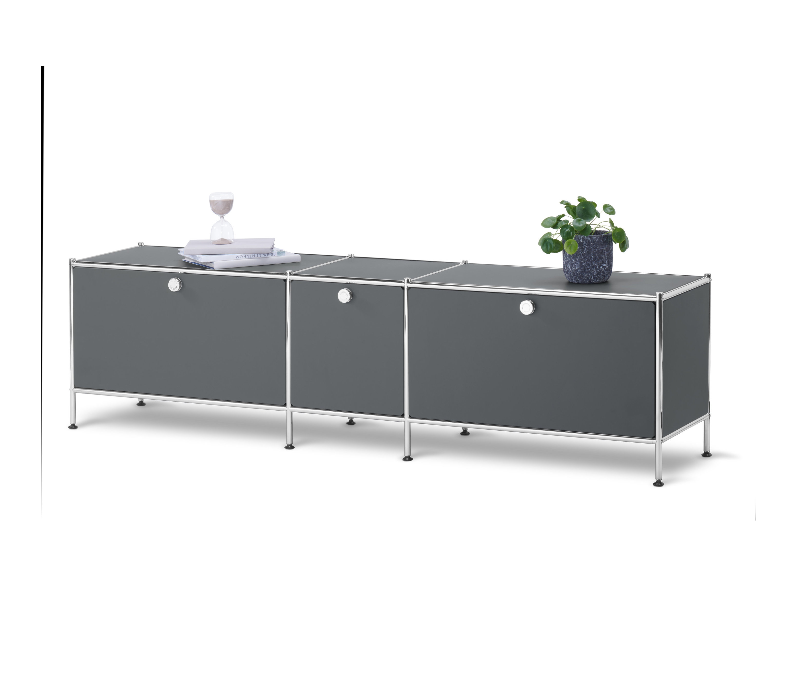 Sivá nízka skrinka »CN3« s 3 výklopnými dvierkami stojí na bielom pozadí. Na skrinke je rastlina v kvetináči, knihy a presýpacie hodiny.