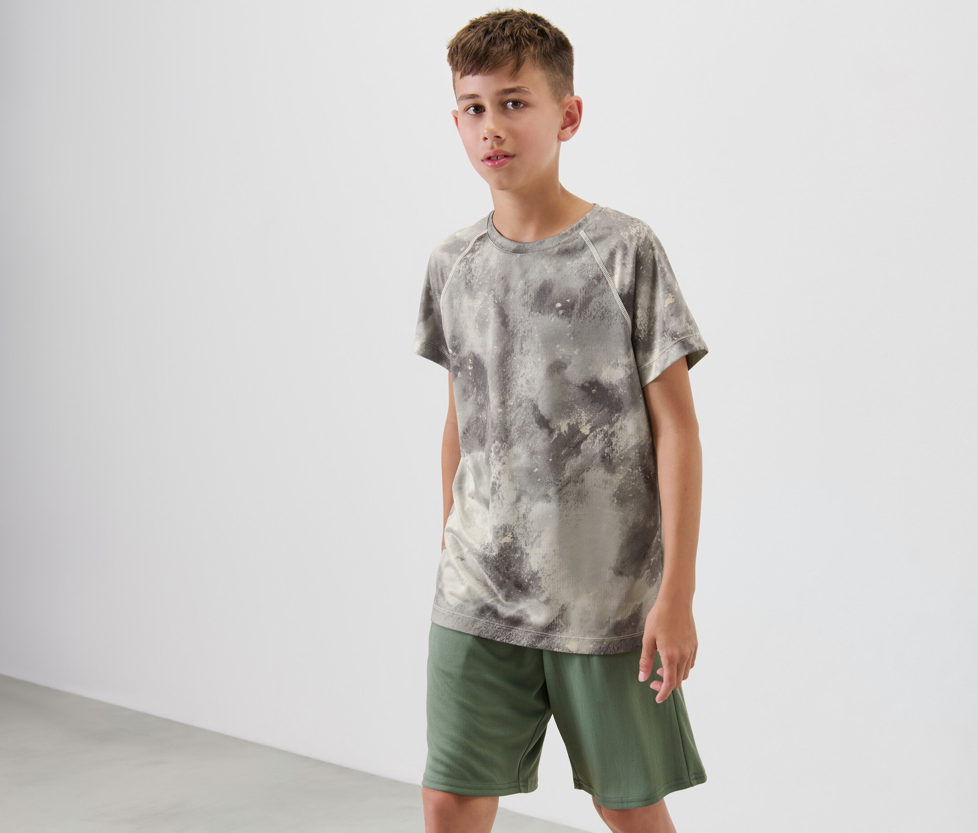 Chlapec stojí a má na sebe zelené detské športové tričko s celoplošnou potlačou.