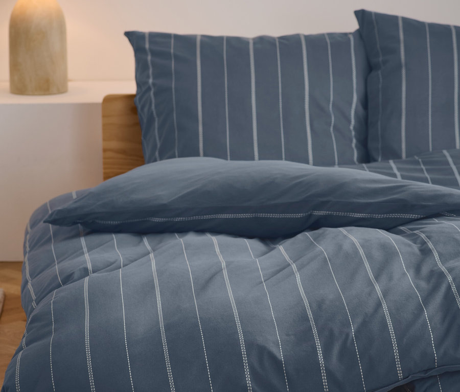 Posteľná bielizeň zo zimného džerseja štandardnej a nadmernej veľkosti s modro-bielym pruhovaným vzorom na posteli.