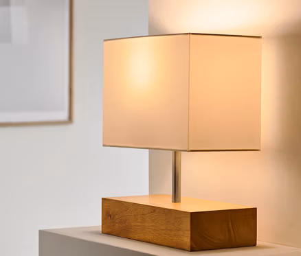 Stolová lampa s dreveným podstavcom stojí na bielom povrchu.
