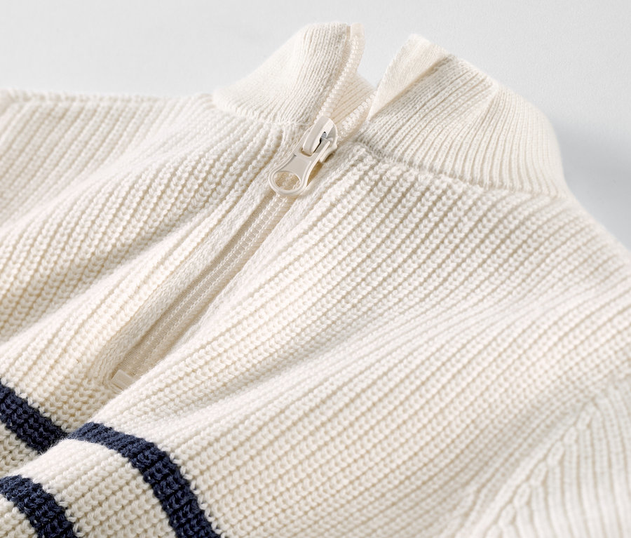 Detailný záber na detský sveter s vysokým golierom na zips s bielym zipsom a tmavomodrými pruhmi.