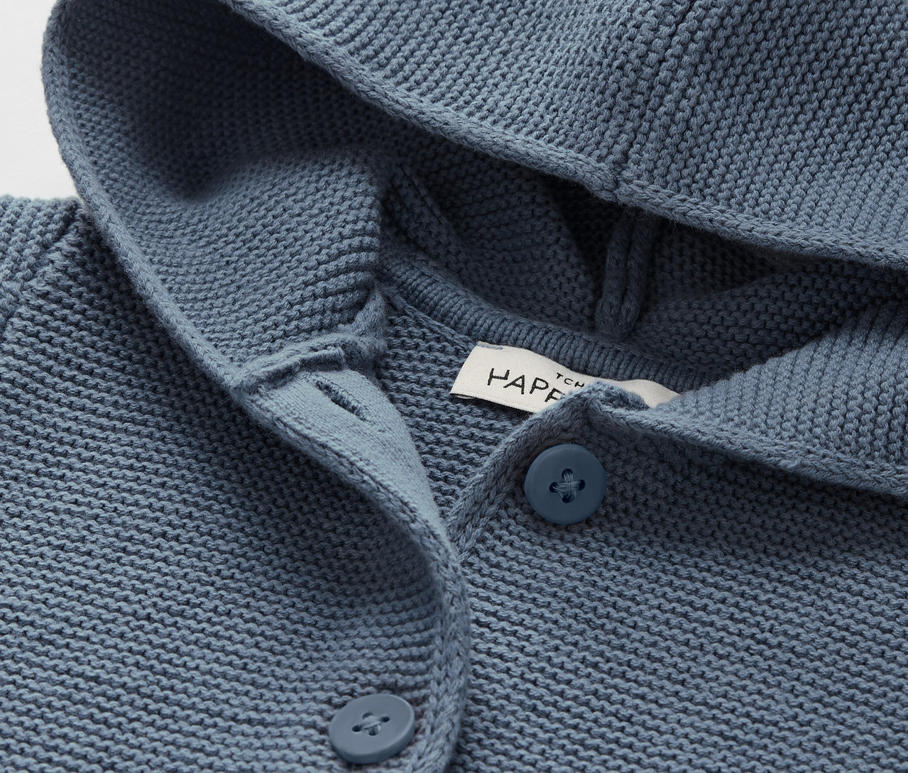 Detail modrého pleteného svetra s kapucňou a gombíkmi.