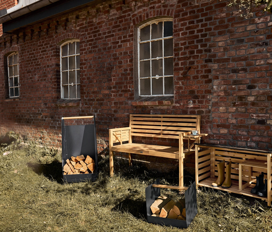 Vonkajší botník, drevená lavica a dva koše na drevo stoja na trávniku pred tehlovou budovou.