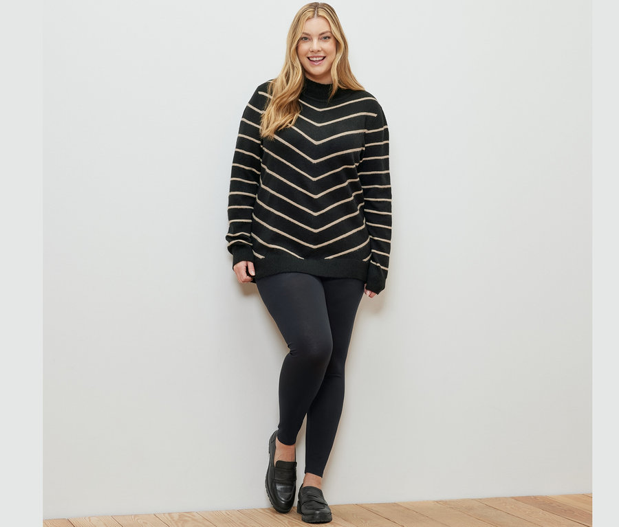 Žena pózuje v čiernom rebrovanom pletenom pulóvri so stojačikom a v legínach.