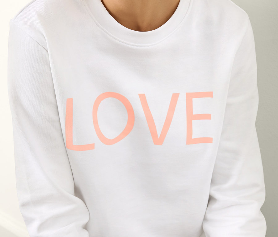 Žena sedí a má na sebe bielu mikinu s potlačou.