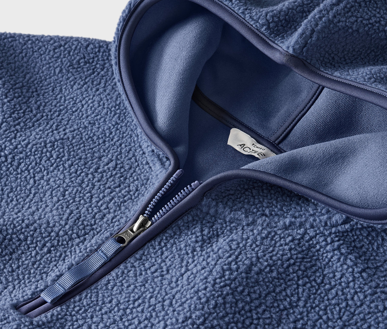 Detail modrej fleecovej mikiny s kapucňou a zipsom.