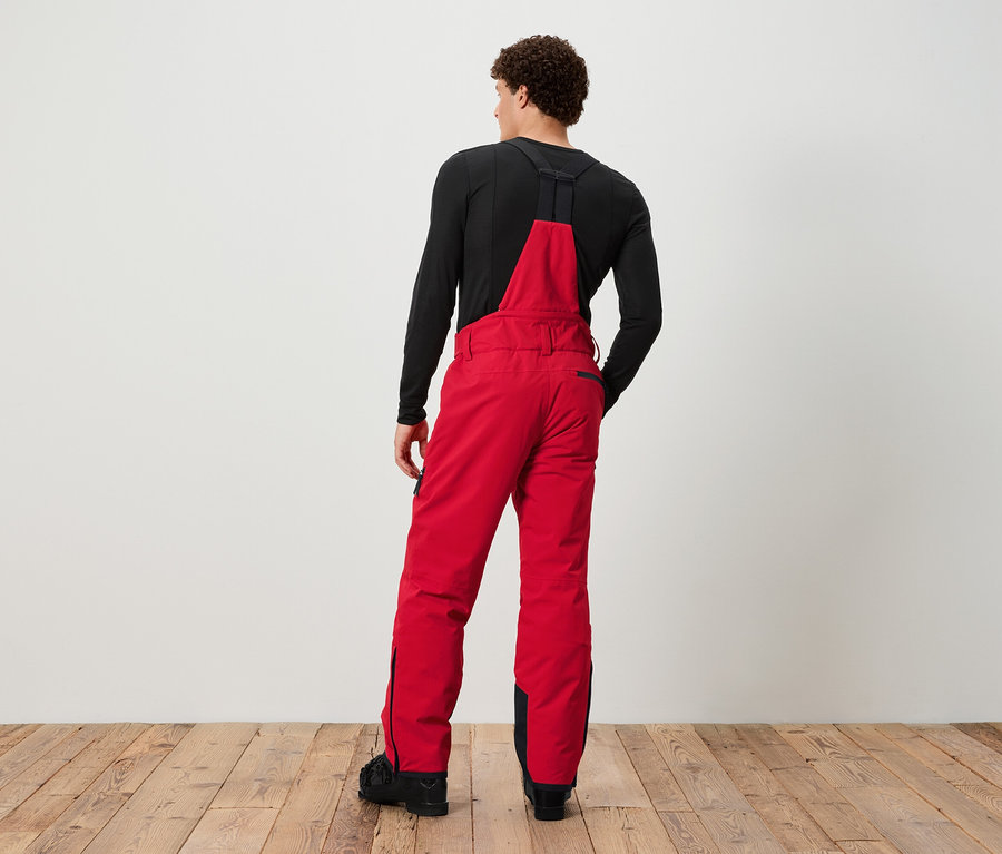 Muž chrbtom k fotoaparátu má na sebe červené lyžiarske nohavice s náprsenkou a čierne tričko.