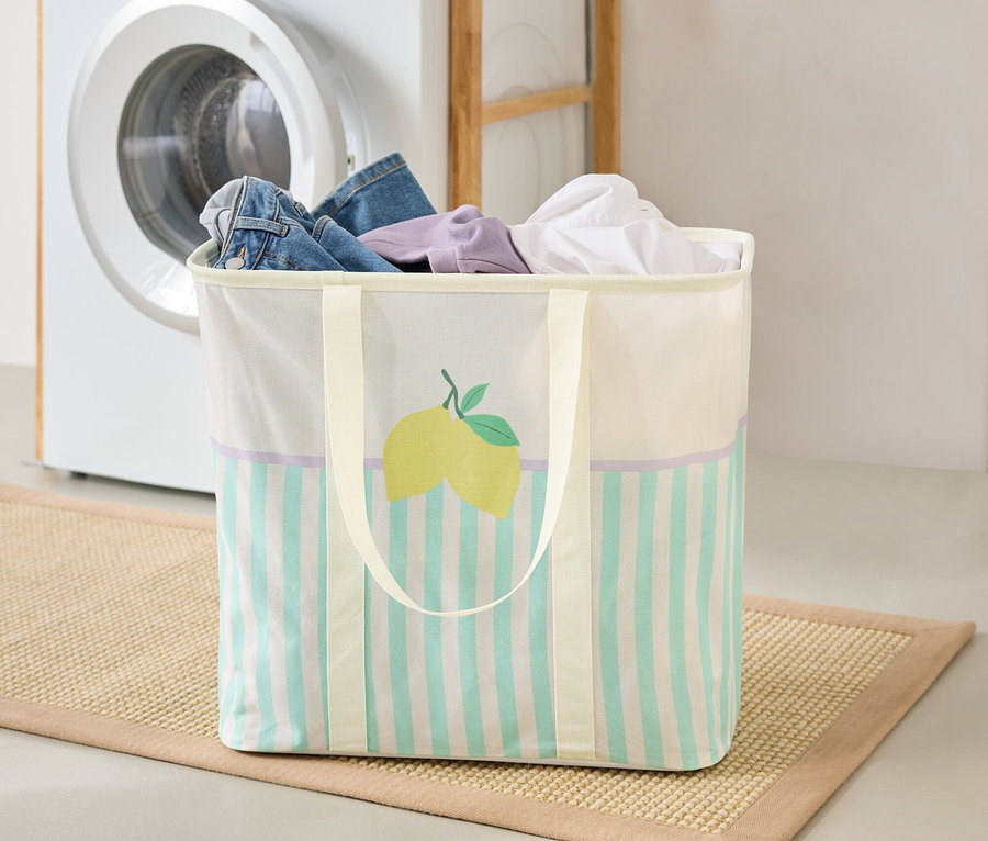 Kôš na bielizeň s motívom citróna stojí na rohožke v práčovni, v pozadí je práčka a regál.