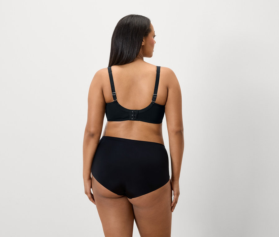 Pohľad zozadu na ženu s tmavými vlasmi v čiernej podprsenke a nohavičkách.